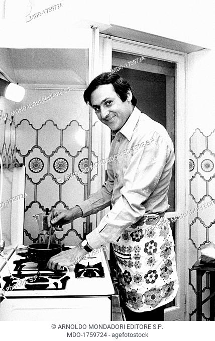 Renzo Arbore blending sauce at burners. The jazzman and broadcast presenter Renzo Arbore at burners in his kitchen, wearing an apron like a perfect housewife