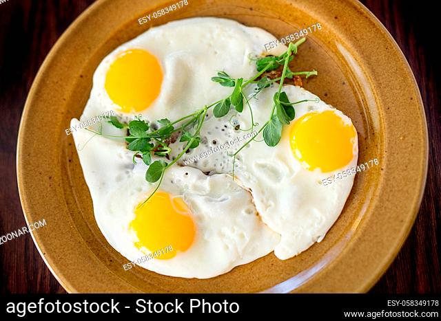 Fried eggs from three chicken eggs with herbs on a plate. Concept - a menu for a cafe. Close-up