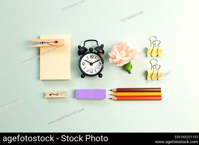 Memo pad, clock, carnation, clip, colored pencil on green background. flat lay, top view, copy space