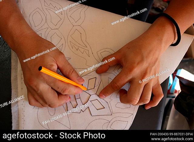 28 April 2020, Mexico, Torreon: A man draws patterns for self-sewn face masks against the corona virus. Since Mexican wrestlers are not allowed to fight in the...