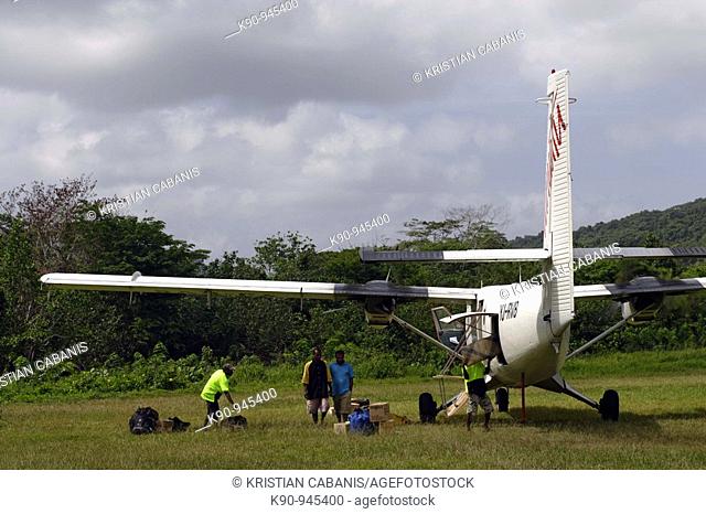 Men offloading and onloading luggage and cargo from a Twin Otter aircraft standing on the grass tarmc of the airport of Sola, Vanua Lava Island, Banks Groups