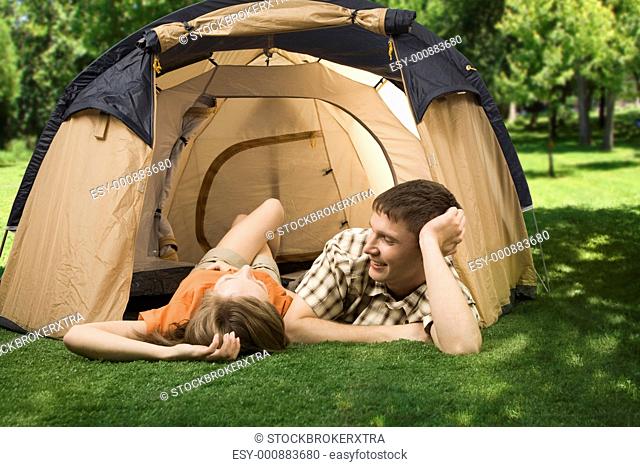 Photo of resting couple lying on green grass in tent and enjoying themselves