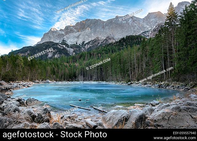 Alpine lake with blue frozen water, surrounded by fir forest and the Alps mountains, near the Eibsee lake, in Bavaria, Germany