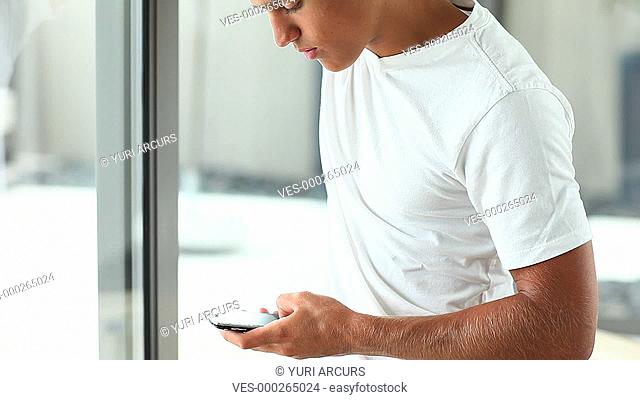 A young man relaxing at home, taking a phone call, while looking out of the window