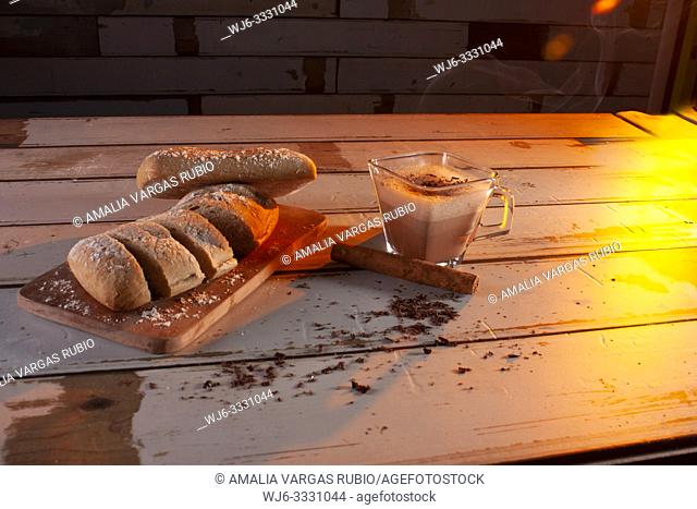 Cup with hot chocolate steaming accompanied by a piece of cinnamon and a baguette finely cut into slices ready for breakfast studio photography with controlled...