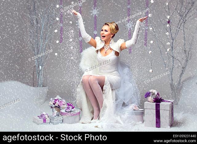 Beautiful happy young bride in felted wedding gown throwing up snow. Present boxes decorated with purple flowers