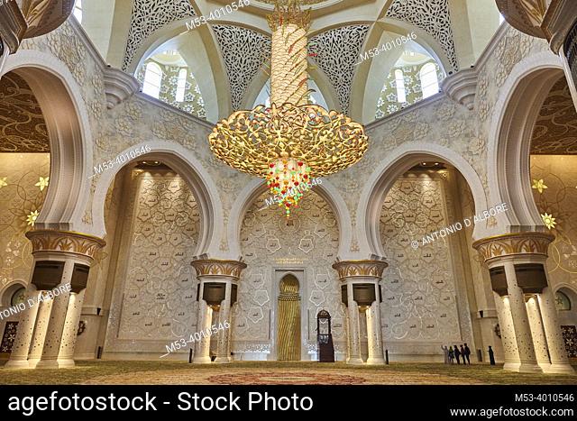 Tourists visiting the prayer room at Sheikh Zayed Mosque. . A very large chandelier hung from the ceiling. Abu Dhabi. United Arab Emirates