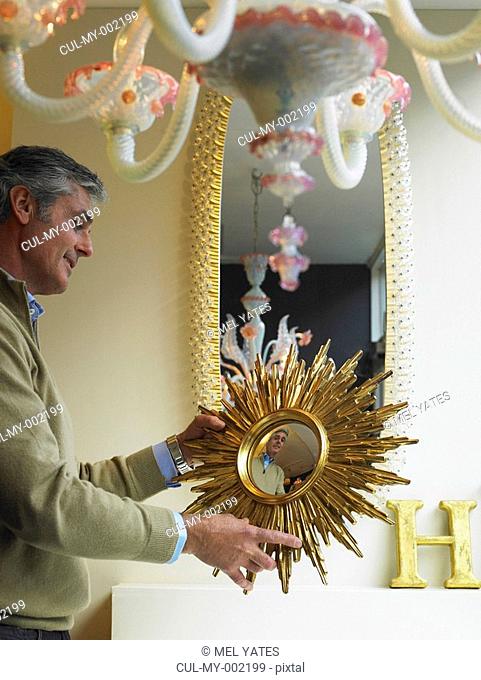 Mature man holding up mirror in shop, smiling