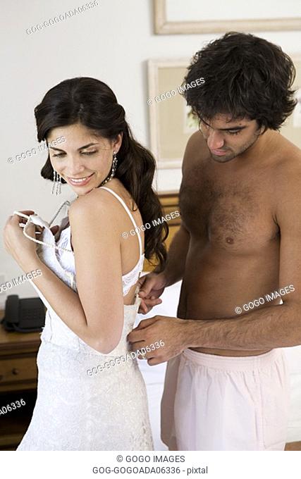 Man unzipping bride's wedding dress
