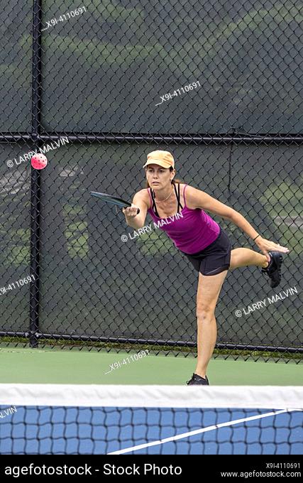 A pickleball player serves the ball on a suburban pickleball court during summer
