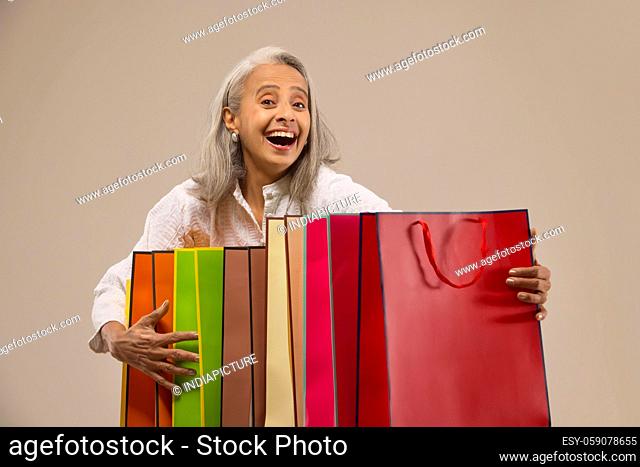 An old woman happily holding colorful carrybags
