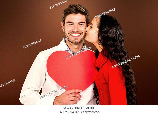 Composite image of man holding paper heart and being kissed by girlfriend
