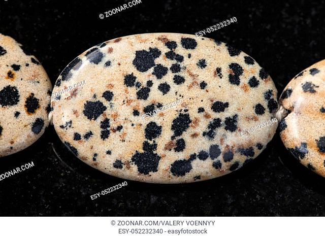 macro shooting of natural mineral rock specimen - necklace from Dalmatian Jasper gemstone on dark granite background
