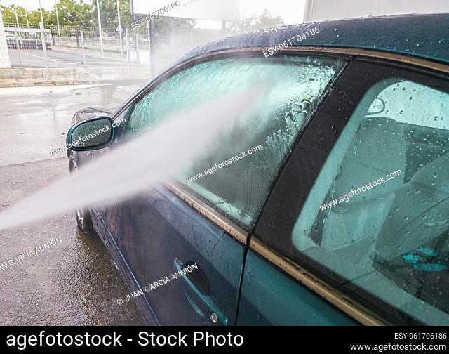 Washing with pressure a dark blue car. Water jet pointing to side windows