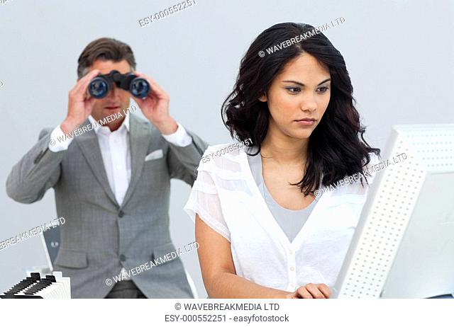 Ambitious businessman looking her colleague's computer through binoculars in the office