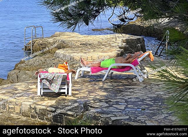 Plava Laguna, Adriatic coast near Porec / Croatia, beach. Vacationers lie on loungers on the stone beach, rocky beach in the sun and chill, relax. ?