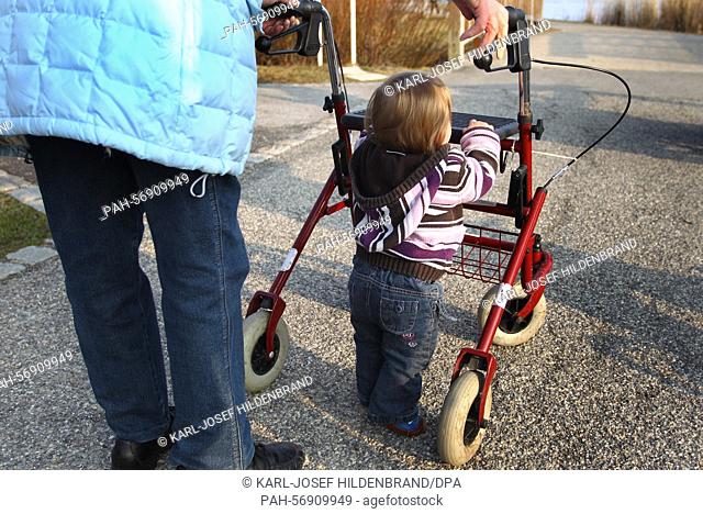 An elderly lady and her eleven-month old grandchild push a walking frame on a sidewalk in Hopferau, Germany, 14 March 2015