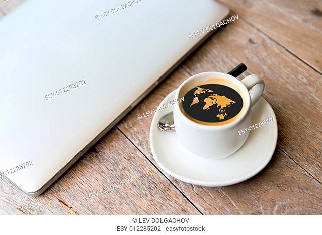 technology, business and modern life concept- close up of open laptop computer and coffee cup with world map silhouette on table at office or hotel room