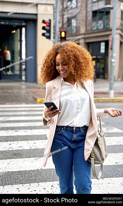 Businesswoman using smart phone crossing city street