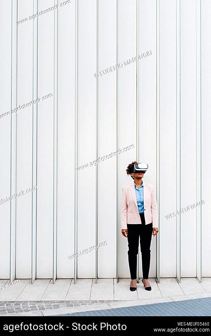 Businesswoman wearing virtual reality simulator in front of white wall
