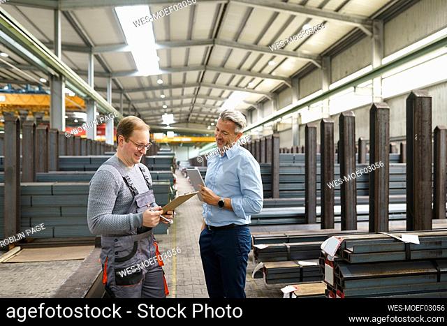 Businessman with tablet and employee with clipboard in factory storehouse