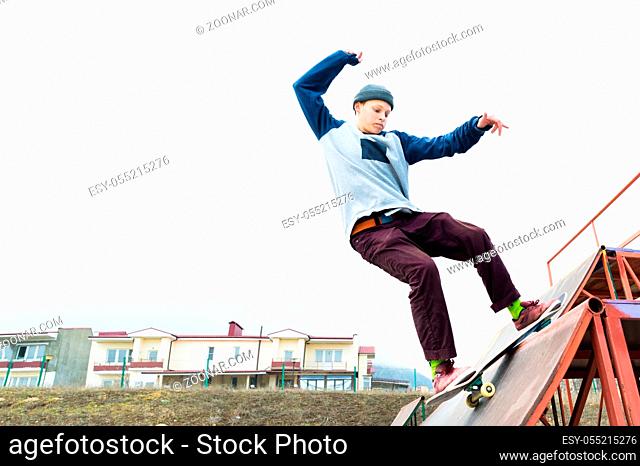 Teen skater in a hoodie sweatshirt and jeans slides over a railing on a skateboard in a skate park, Wide angle