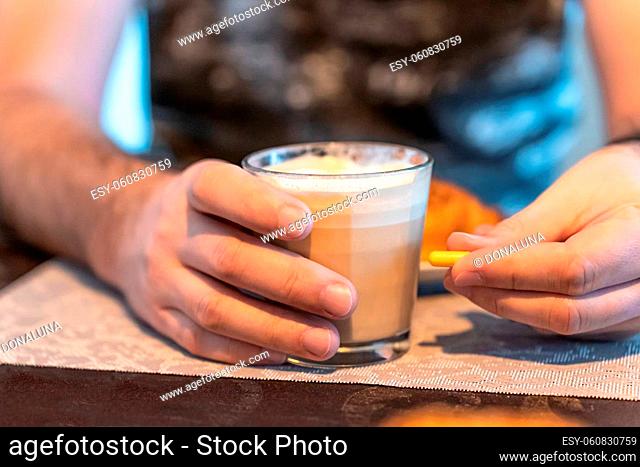 Selective focus on a man's hands, a glass of coffee in one hand and a capsule of medication in the other