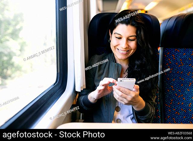 Happy woman using smart phone while sitting in train
