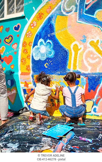 Girls painting vibrant mural on sunny wall