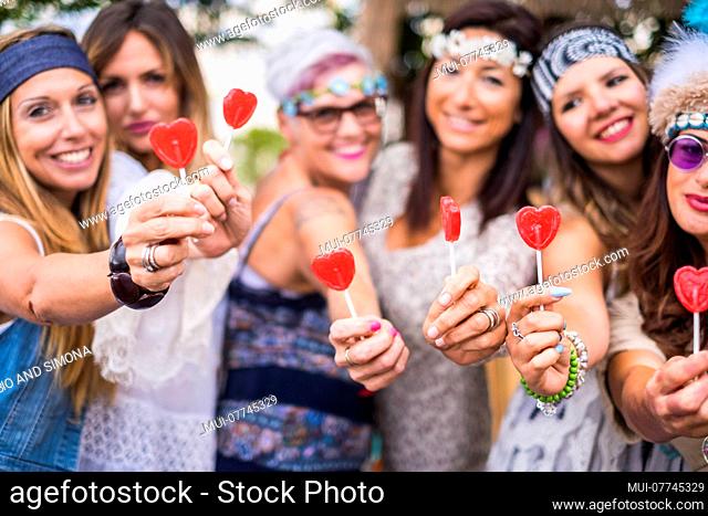 group of mixed ages women from young to old stay together in friendship taking and offering a candy hearth lollypop to you