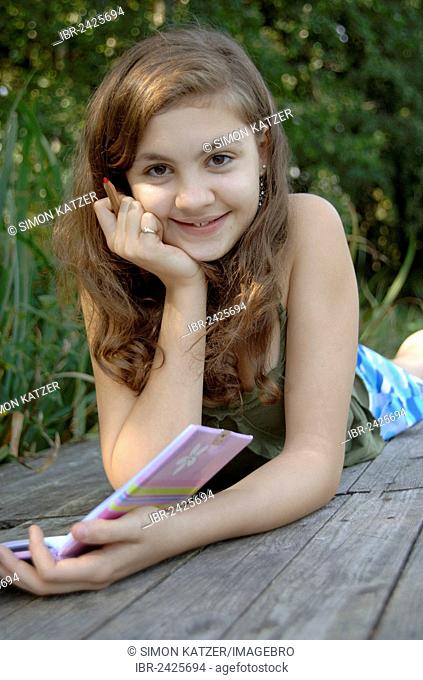 Teenage girl lying on a boardwalk with a book and a pen in her hand