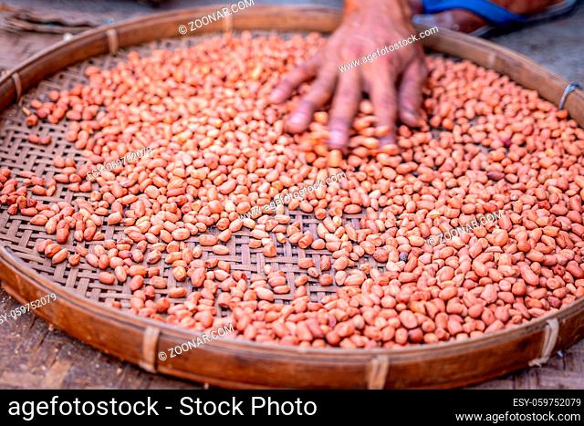 Hands on shelled peanuts in a threshing basket at a local market