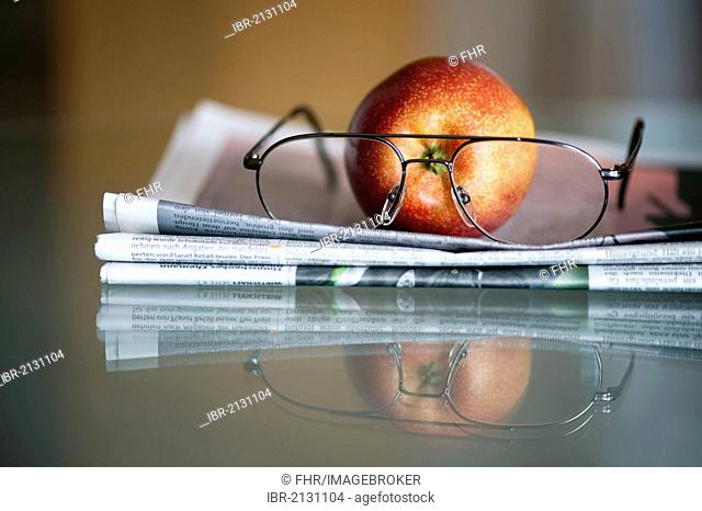 Apple, newspaper and glasses lying on a glass table