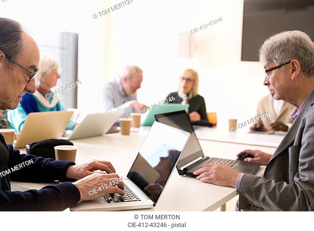Senior businessmen using laptops in conference room meeting