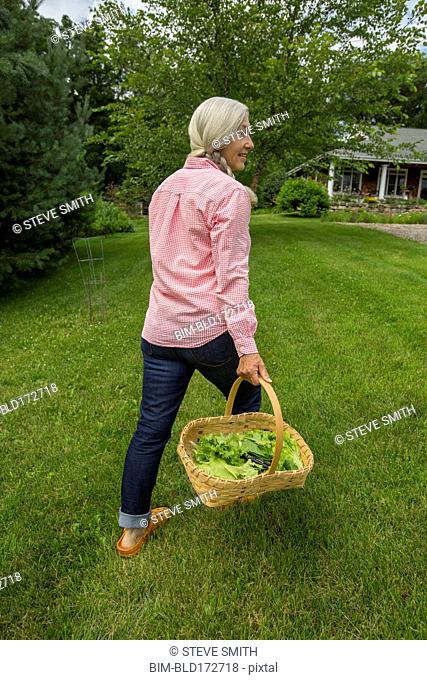 Caucasian woman carrying basket of vegetables in backyard