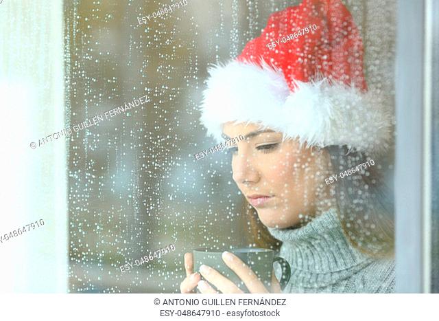 Sad woman in christmas looking down through a windos in a rainy day