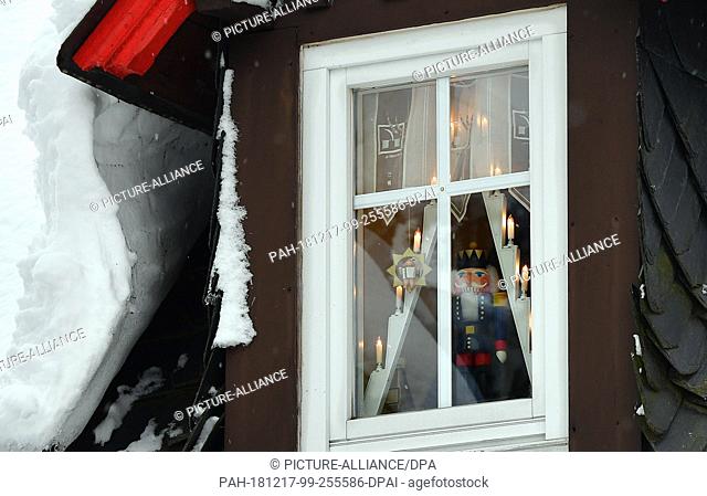 15 December 2018, Saxony, Seiffen: A nutcracker stands behind a snow-covered roof window in the toy village Seiffen. During Advent Seiffen is considered a...