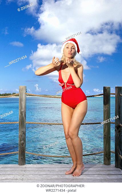 woman in New Year's Santa-Klaus cap on background of ocean jumps and sends an air kiss