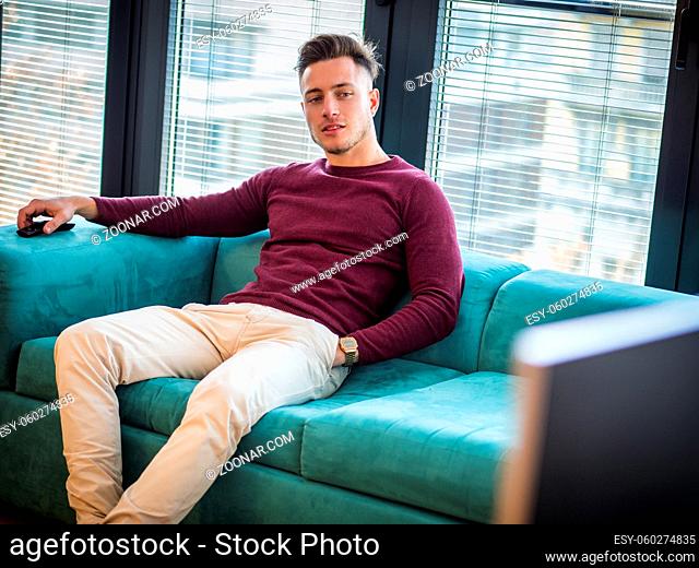 Young man sitting watching television changing the channel with the remote control