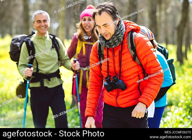 Man wearing binoculars trekking with friends in forest