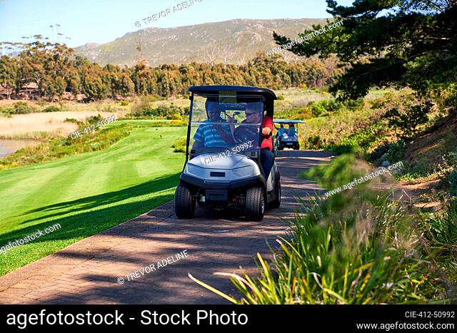 Male golfers riding in golf cart on sunny golf course path