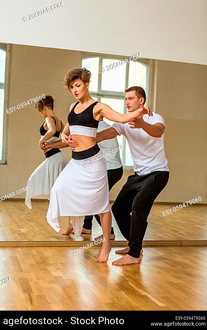 beautiful couple dancing tango. young woman in black and white dress and man in sport clothes practicing in dancing studio mirror room. copy space