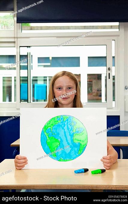 Primary school caucasian girl holding placard with an image of the earth themes of drawing protection environment