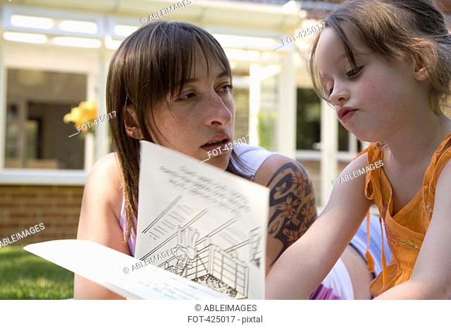 Mother and daughter reading a book together in a backyard
