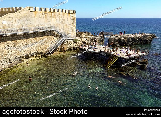 Sunbathers on a sunny platform above the sea in Siracusa, Sicily, Italy