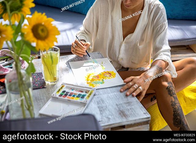 Artist painting with brush sitting near table at home