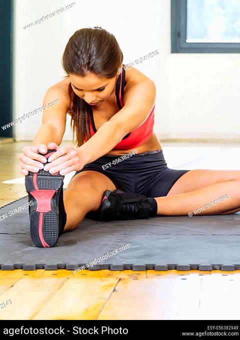 Beautiful woman stretching her leg muscles on the floor sitting on a mat.