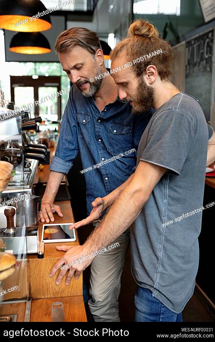 Coffee shop owner sharing tablet PC with barista in cafe