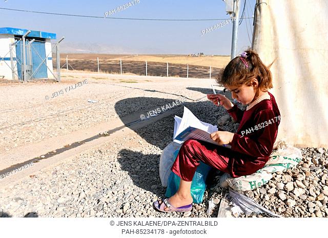 A girl sits with a schoolbook for math and studies by her family's tent in the Mamilian refugee camp in the Dohuk region, Iraq, 19 October 2016
