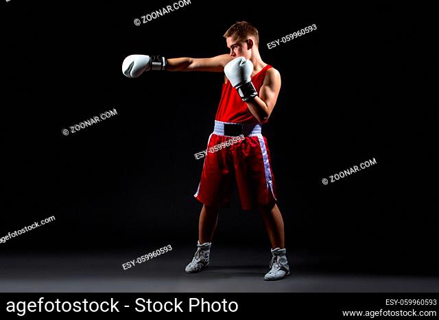 Young handsome boxer sportsman in red boxer suit and white gloves standing on black backgound. Copy space